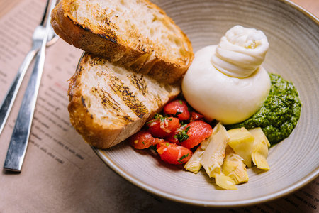 fresh vegetables salad with white soft burrata cheese and green pesto close up