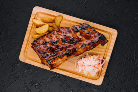 Pork loin ribs served on chopping board and potato wedgesの写真素材