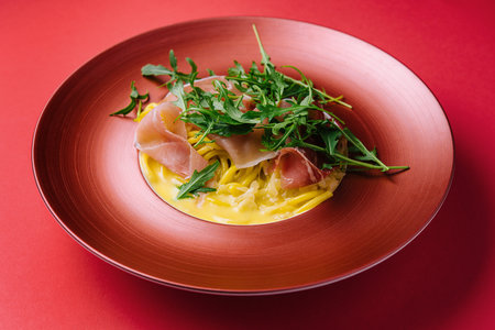 spaghetti with prosciutto and arugula on red plateの写真素材