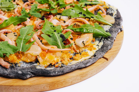 Black pizza with seafood on a wooden round plate on a whiteの写真素材