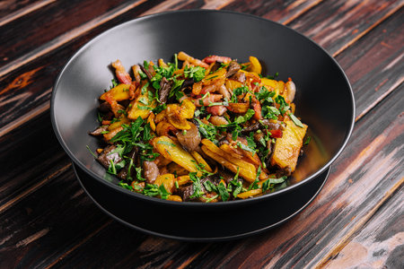 Fried potatoes with mushrooms on a black plate