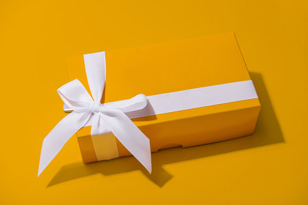 Yellow gift box with white ribbon isolated on yellowの写真素材