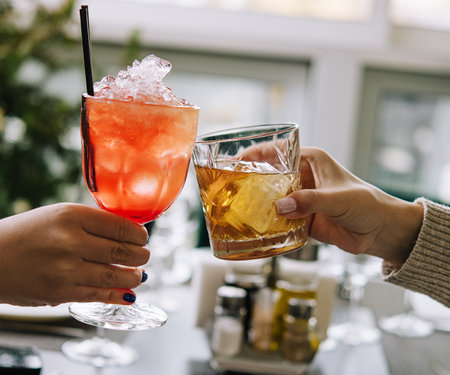 Friends toasting with glasses of whiskey and strawberry cocktailの写真素材