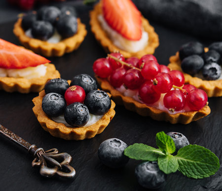 Delicious tartlets with fruit and cream mascaropne on black boardの写真素材