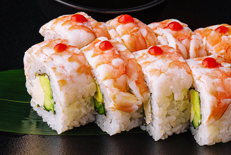 Sushi roll covered with shrimp meat on black ceramic plateの写真素材