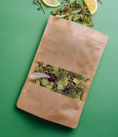 Leaf tea spilled out of a paper packet with orange slices on green background