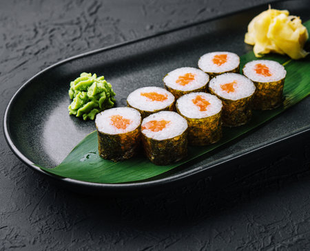 Row of fresh maki sushi rolls on black plateの写真素材