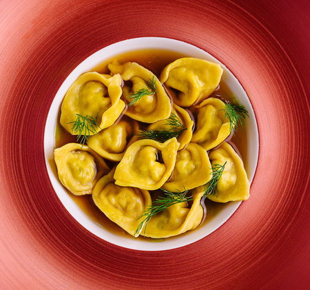 Filled tortellini with herbs on red plateの写真素材