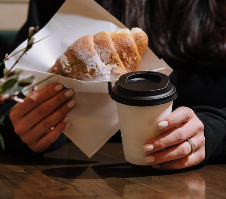 Woman holding a mug of coffee and a croissantの写真素材