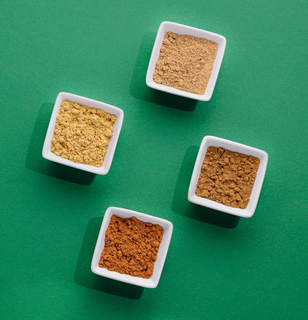 Various Indian Spices in Small White Bowls on green background
