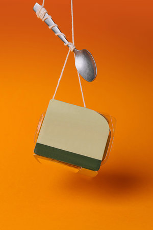 Conceptual still life image of takeaway breakfast and spoon hanging against a vibrant orange backdropの写真素材