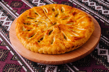 Freshly baked georgian cheese bread, khachapuri, served on a wooden board with an ethnic patterned backgroundの写真素材