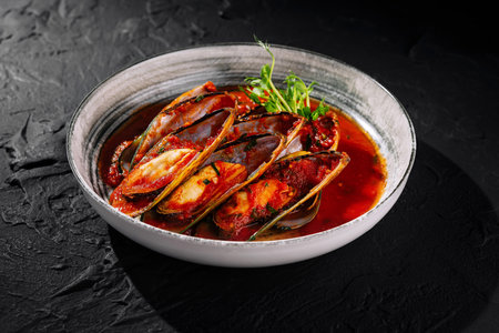 Savory dish of mussels in spicy tomato sauce garnished with fresh herbsの写真素材