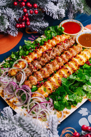 Vibrant dish of spiced meat skewers served with onions, herbs, and sauces on a festive tableの写真素材