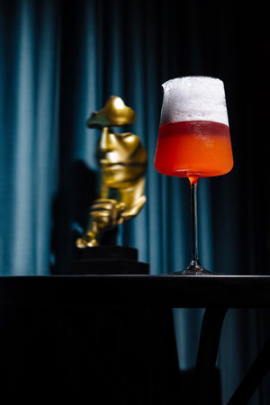 Vibrant cocktail in a tall glass stands out against a moody, dark backdrop with a blurred statue figureの写真素材