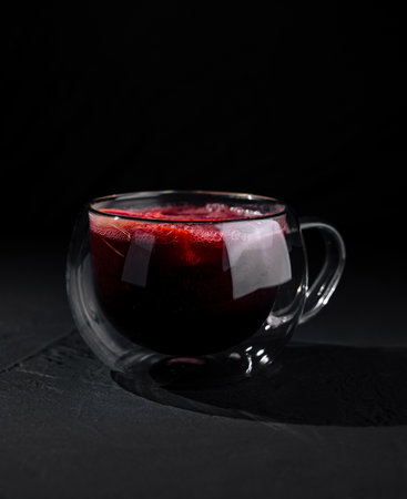 A modern double-walled glass cup filled with red tea, isolated on a dark, moody backdropの写真素材