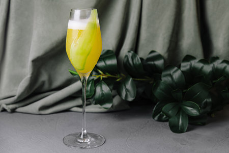 Chic yellow cocktail in a tall champagne glass, garnished with a lemon, against a gray backdropの写真素材