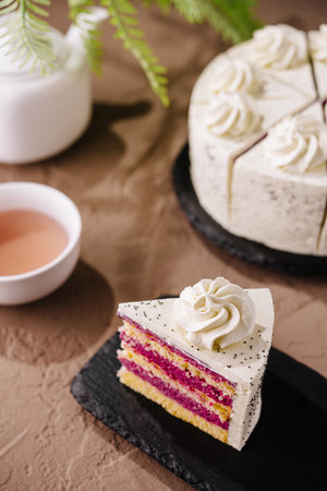Elegant slice of layered cake with cream frosting and poppy seeds, served on a slate plate