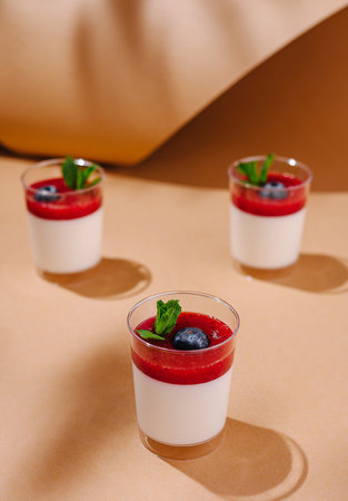 Three glasses of creamy panna cotta with vibrant red berry coulis, blueberries, and mint, artfully arrangedの写真素材