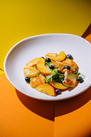 Halloumi and peach salad with blueberries served on a white plate with a dual-tone backgroundの写真素材