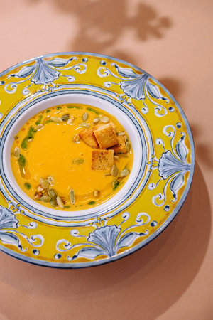 Top-down view of a colorful bowl with creamy pumpkin soup, garnished with seeds and croutons