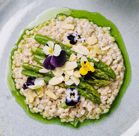 Exquisite plate of risotto garnished with fresh asparagus and colorful edible flowers, artfully presentedの写真素材