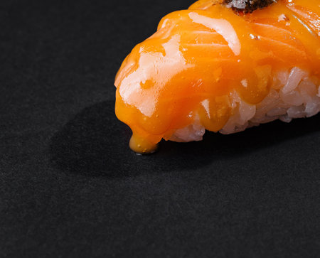 Close-up of a delicious salmon nigiri sushi garnished with a small dab of wasabi on a dark backdropの写真素材