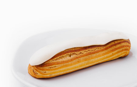 Freshly baked eclair with creamy filling on a clean white plate isolated on white backgroundの写真素材