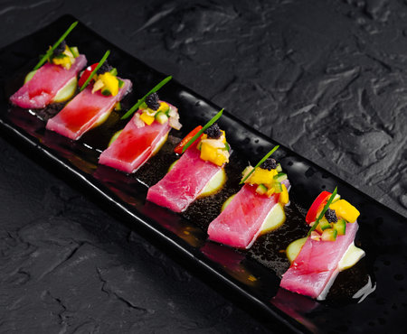 Elegant presentation of tuna sashimi garnished with mango and avocado on a dark slate platterの写真素材