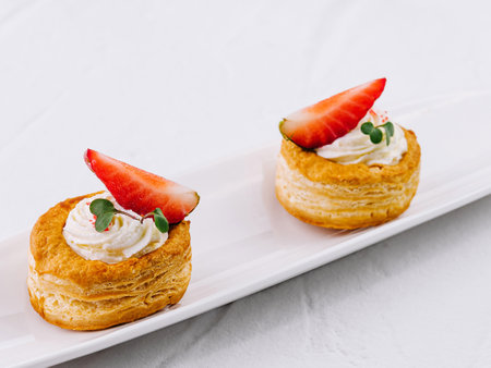 Delicious puff pastry desserts with cream and fresh strawberries on a sleek white plateの写真素材
