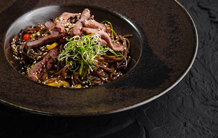 Savory stir-fried beef with vegetables on a stylish dark plate, set against a black backgroundの写真素材