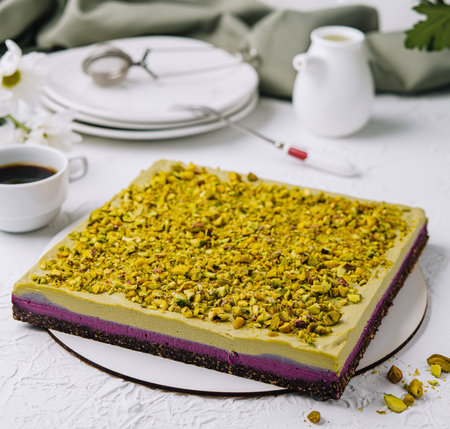 Delicious pistachio cake paired with coffee on a white table, complemented by fresh flowersの写真素材