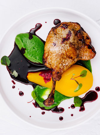 Elegant plate of roasted chicken with vibrant green and yellow purees, drizzled with berry reductionの写真素材
