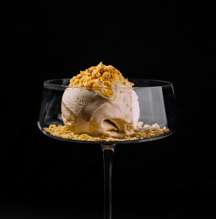 Artfully plated ice cream dessert with crumble topping in a stylish coupe glass on a dark background