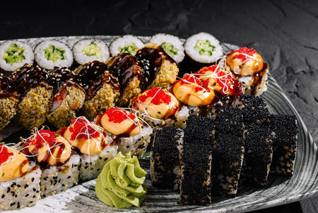 Luxurious variety of sushi rolls served with wasabi and ginger on a sleek plate against a dark backdropの写真素材