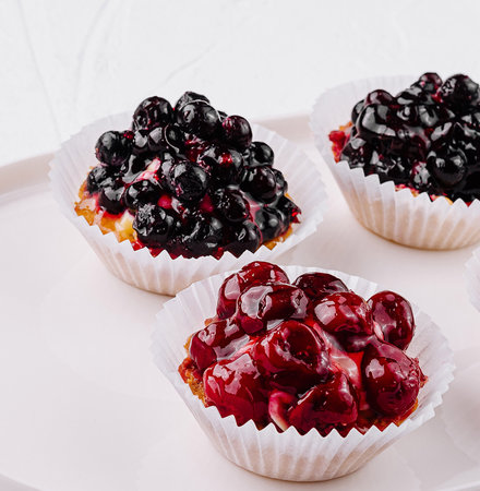 Delicious mini tartlets filled with fresh berries, displayed on a sleek white plateの写真素材