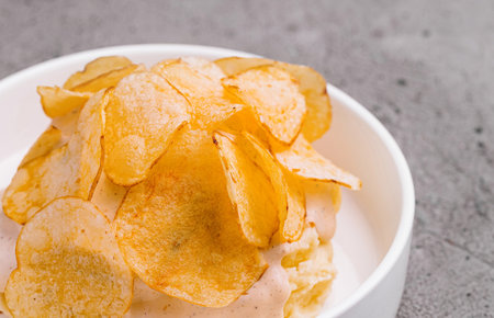 Appetizing potato chips served in a white bowl on a textured gray background