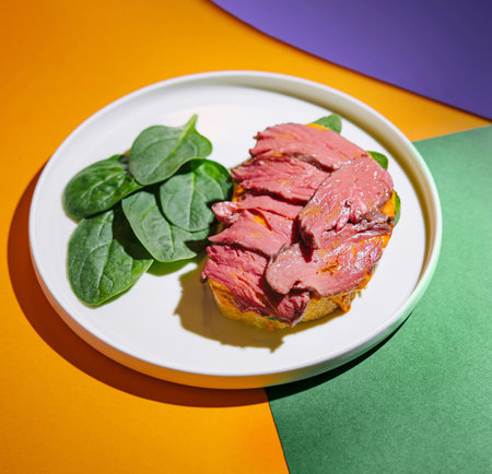 Sliced roast beef on a bed of spinach served on a white plate, vibrant background