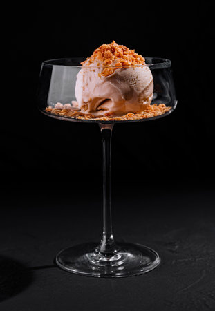 Artfully plated ice cream dessert with crumble topping in a stylish coupe glass on a dark backgroundの写真素材