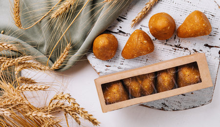 Freshly baked bread rolls in a box beside wheat sheaves on a wooden table with a clothの写真素材