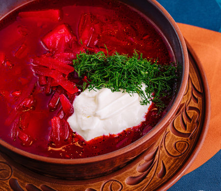 Vibrant bowl of traditional borscht garnished with sour cream and dill on a patterned tableclothの写真素材