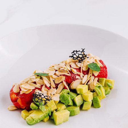 Fresh avocado salad with bell pepper and nuts and slivered almonds on a white plateの写真素材