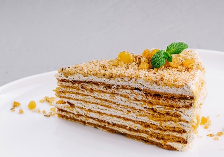 Elegant slice of multi-layered honey cake garnished with mint, served on a sleek white dishの写真素材