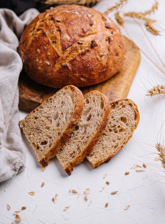 Freshly baked sourdough bread with slices on a board, decorated with wheat ears on a white table