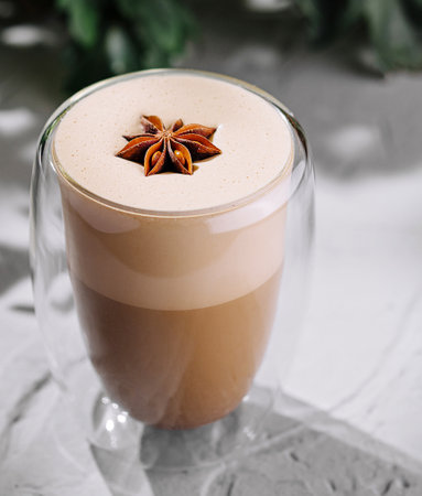 Elegant glass of creamy spiced latte garnished with a star anise on a modern textured table