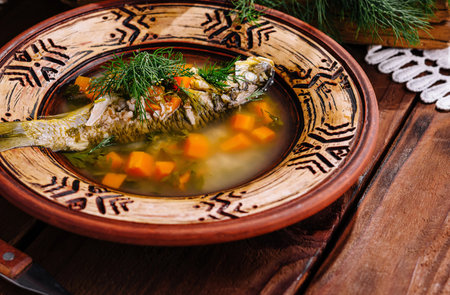 Appetizing homemade fish soup in a clay bowl with fresh dill on a wooden tableの写真素材