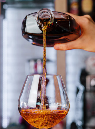 Bartender pouring golden whiskey into an elegant glass on a vibrant bar counterの写真素材