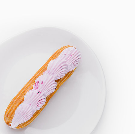 Top view of a delicious eclair with pink icing on a clean white plate, isolated on white backgroundの写真素材