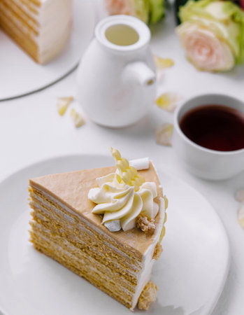 Delectable slice of layered cake with creamy frosting on a white background, paired with tea