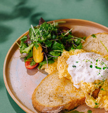 Healthy breakfast meal of scrambled eggs, toast, and fresh salad served on a rustic plate with a green backgroundの写真素材